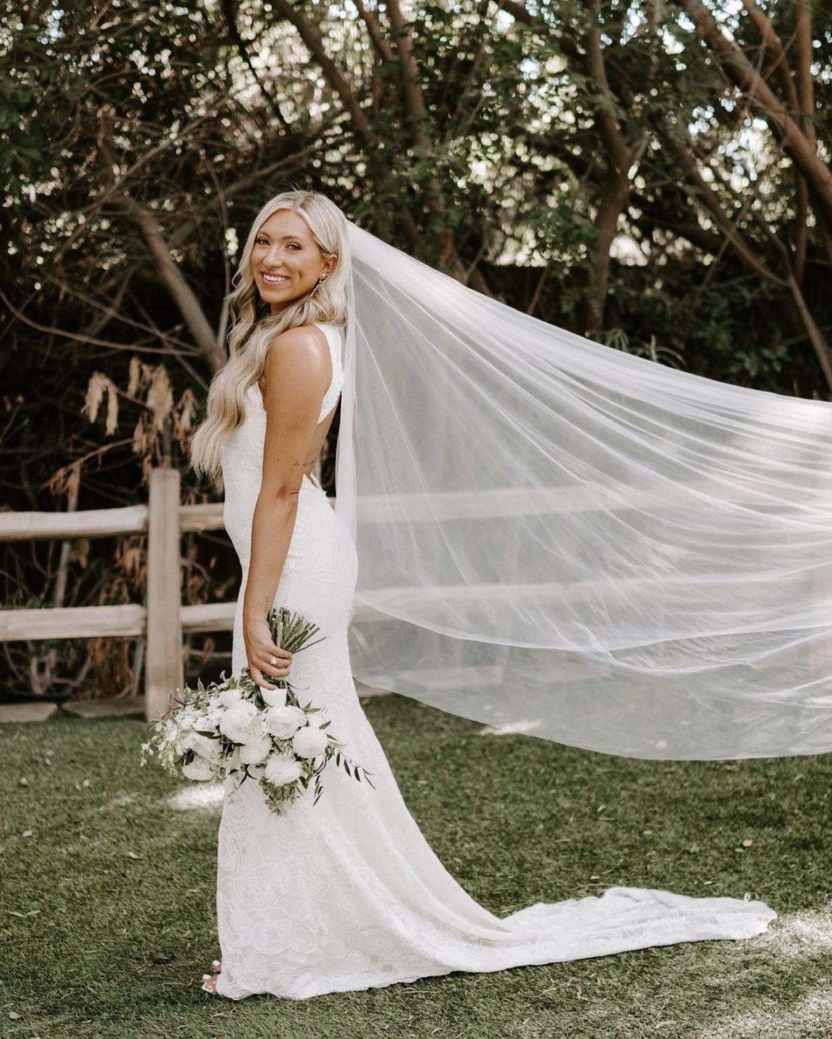 Smiling bride with long blonde waves, natural glam makeup and a flowing cathedral veil