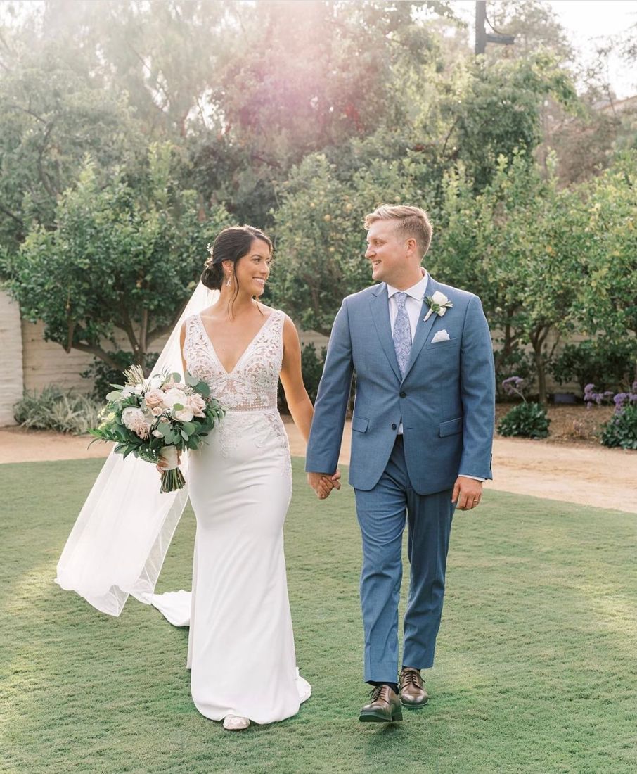Bride with a low bun and natural makeup walking with her groom in a garden