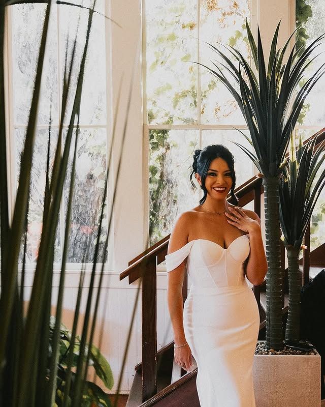 Bride in an off-shoulder gown with a low updo, smiling on a staircase