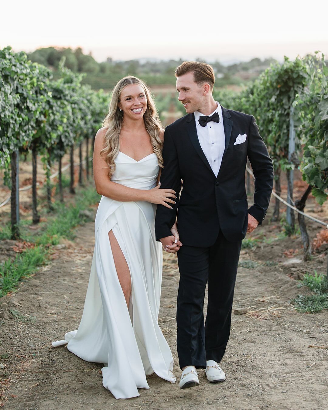 Bridal hair: long soft waves on a bride walking through a vineyard with her groom